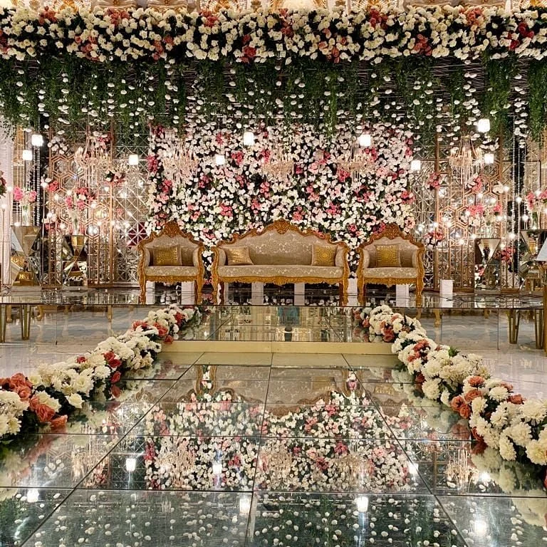 An Oriana wedding stage with a full floral wall and mirrored floor